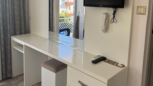 A hotel room with a white desk, a mounted flat-screen TV, a telephone, and an air conditioning unit. - Send Apart Otel (Konyaalti)