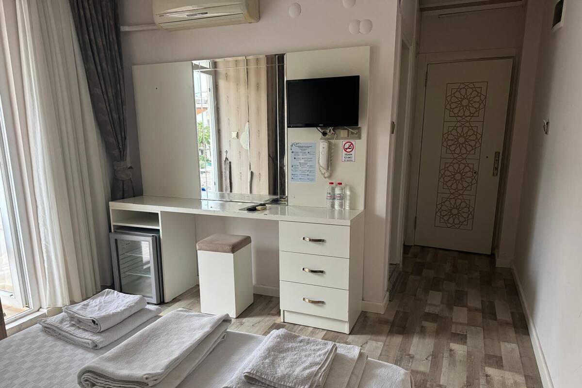 Une chambre d’hôtel équipée d’un bureau, d’un miroir, d’un petit réfrigérateur, d’une coiffeuse avec des tiroirs et d’un lit agrémenté de serviettes soigneusement pliées.