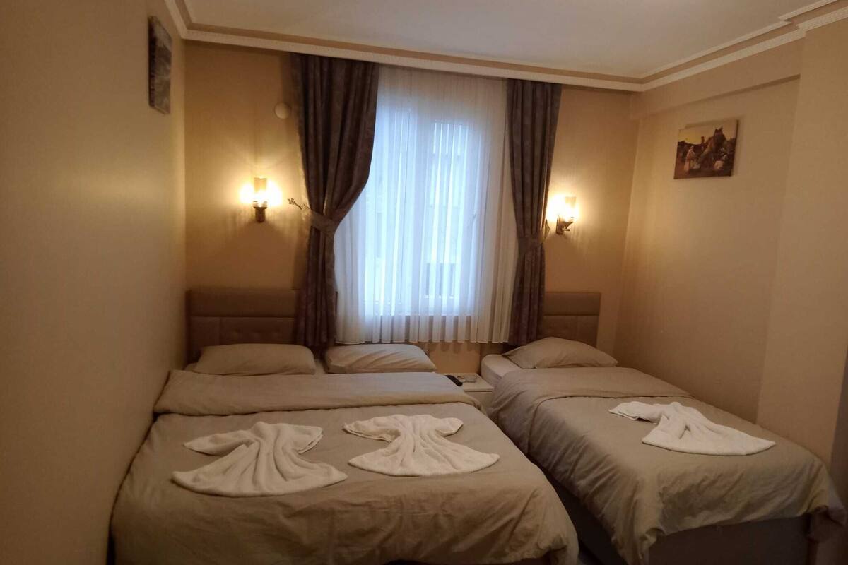 Une chambre d’hôtel avec deux lits, chacun doté d’une tête de lit et d’une table de chevet. Deux lampes murales sont fixées de part et d’autre de la fenêtre.