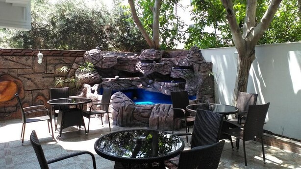 An outdoor patio with a stone waterfall feature, wicker furniture, and a view of surrounding greenery. - Send Apart Otel (Konyaalti)