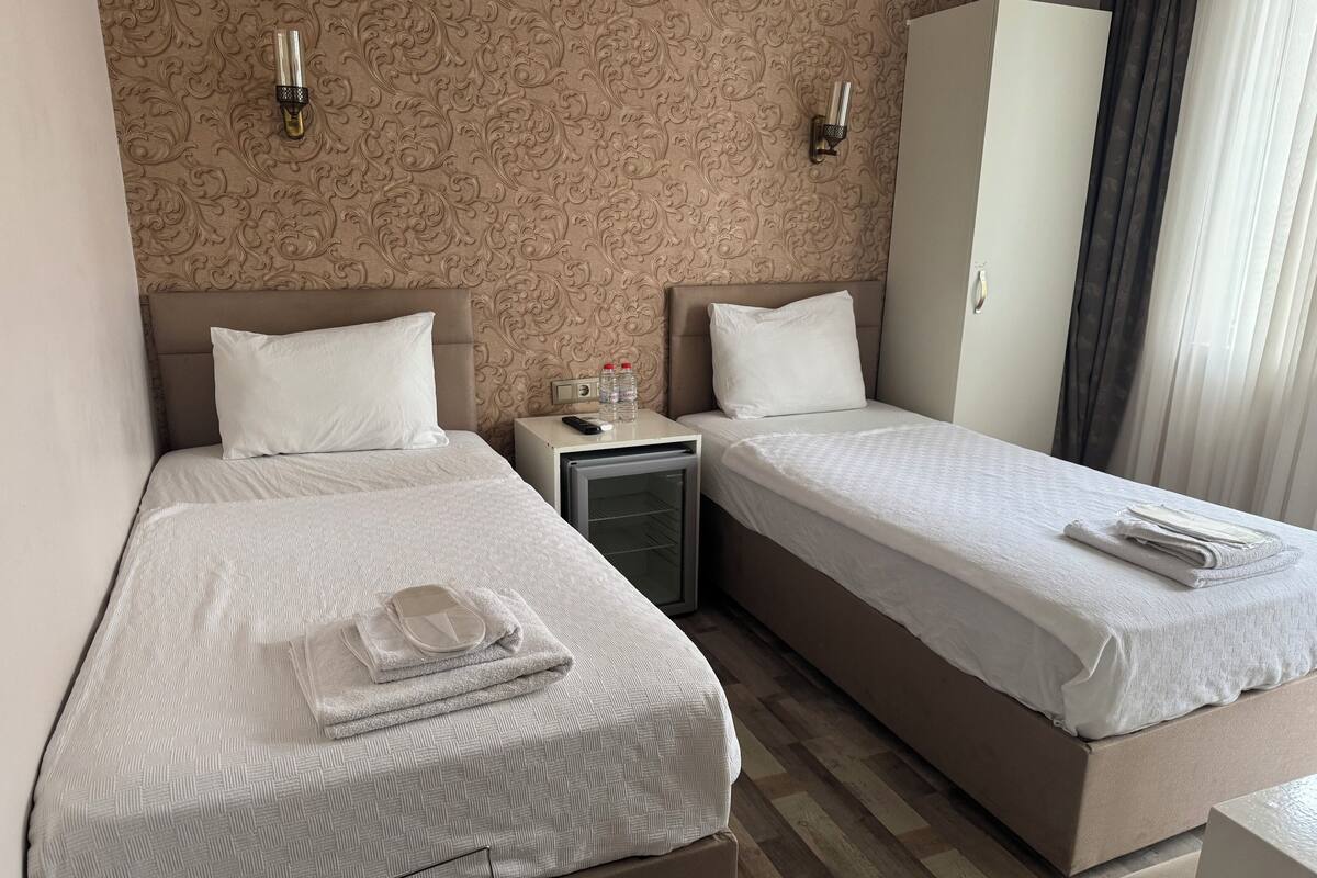 Une chambre d’hôtel avec deux lits, une armoire, une table de chevet avec une télécommande et un mini-bar.