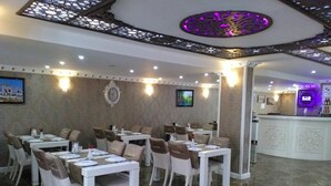 A restaurant with white tables and chairs, a bar area, and a patterned carpet. - Send Apart Otel (Konyaalti)