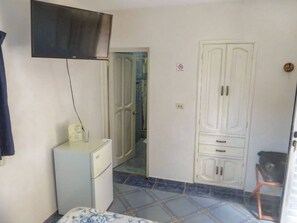 Compact room with a tiled floor, featuring a refrigerator, flat-screen TV, and a wardrobe.