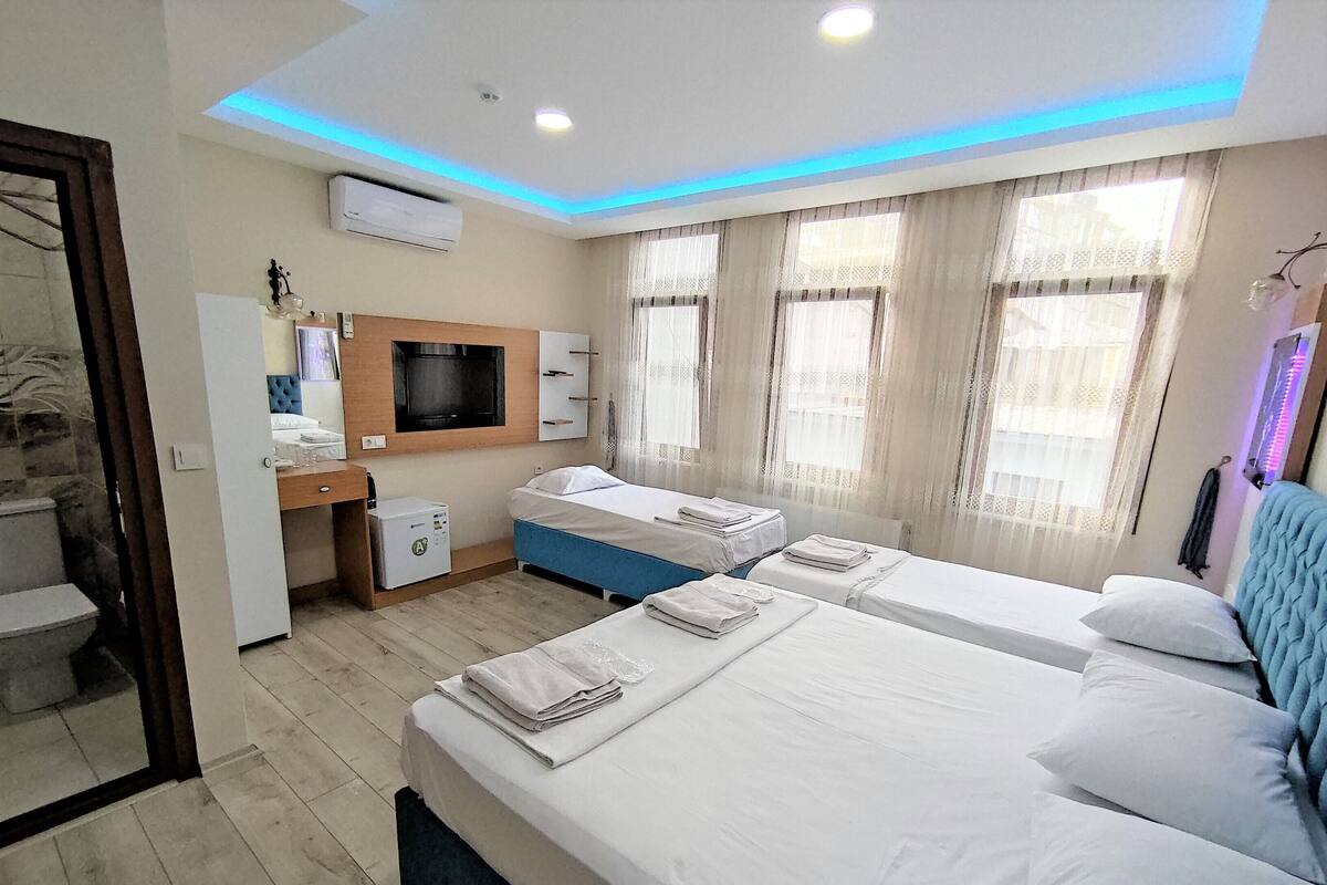 A hotel room with two beds, a desk, a TV, and a window with curtains.