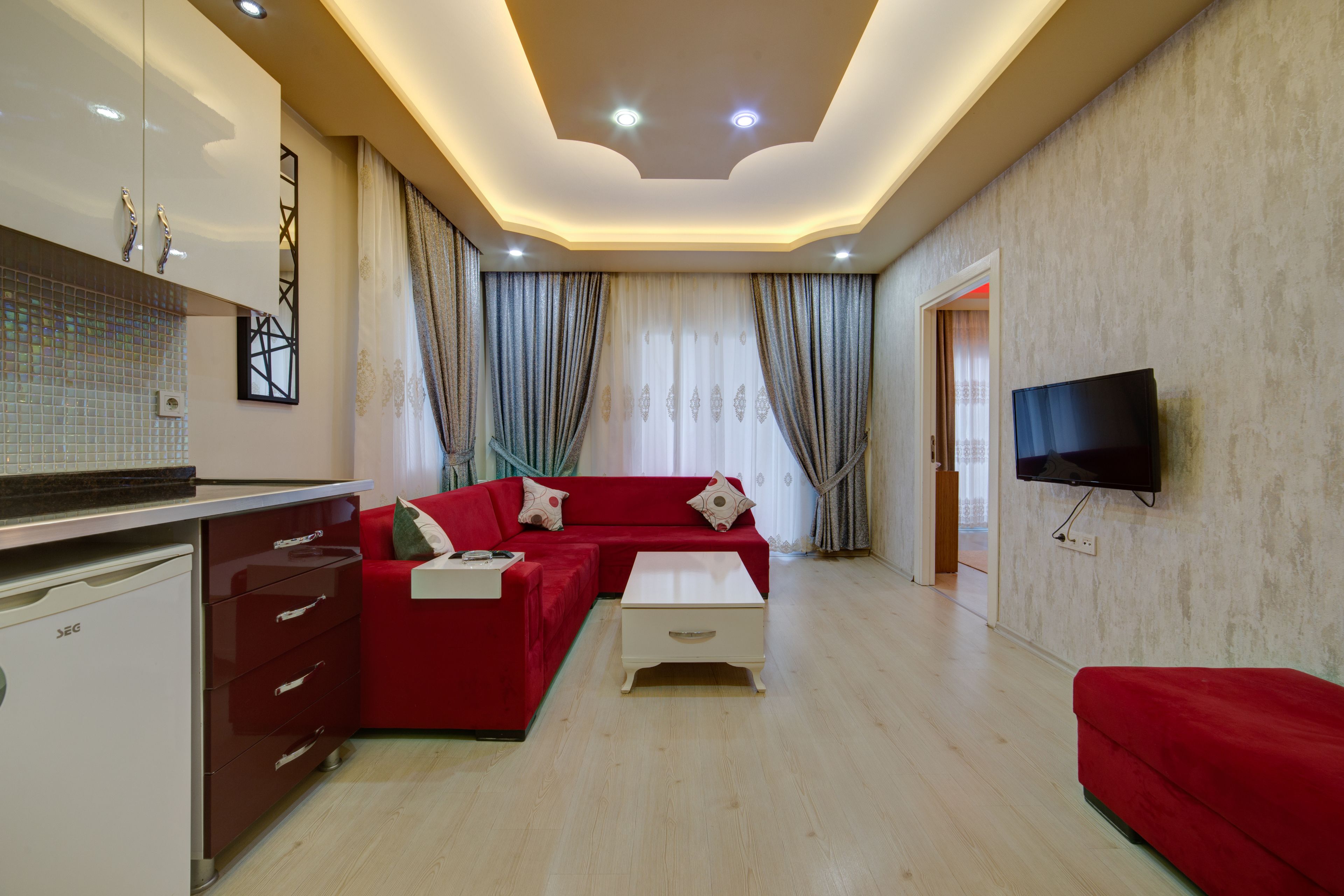 A modern living room with a red sofa, a white coffee table, and a flat-screen TV mounted on the wall.