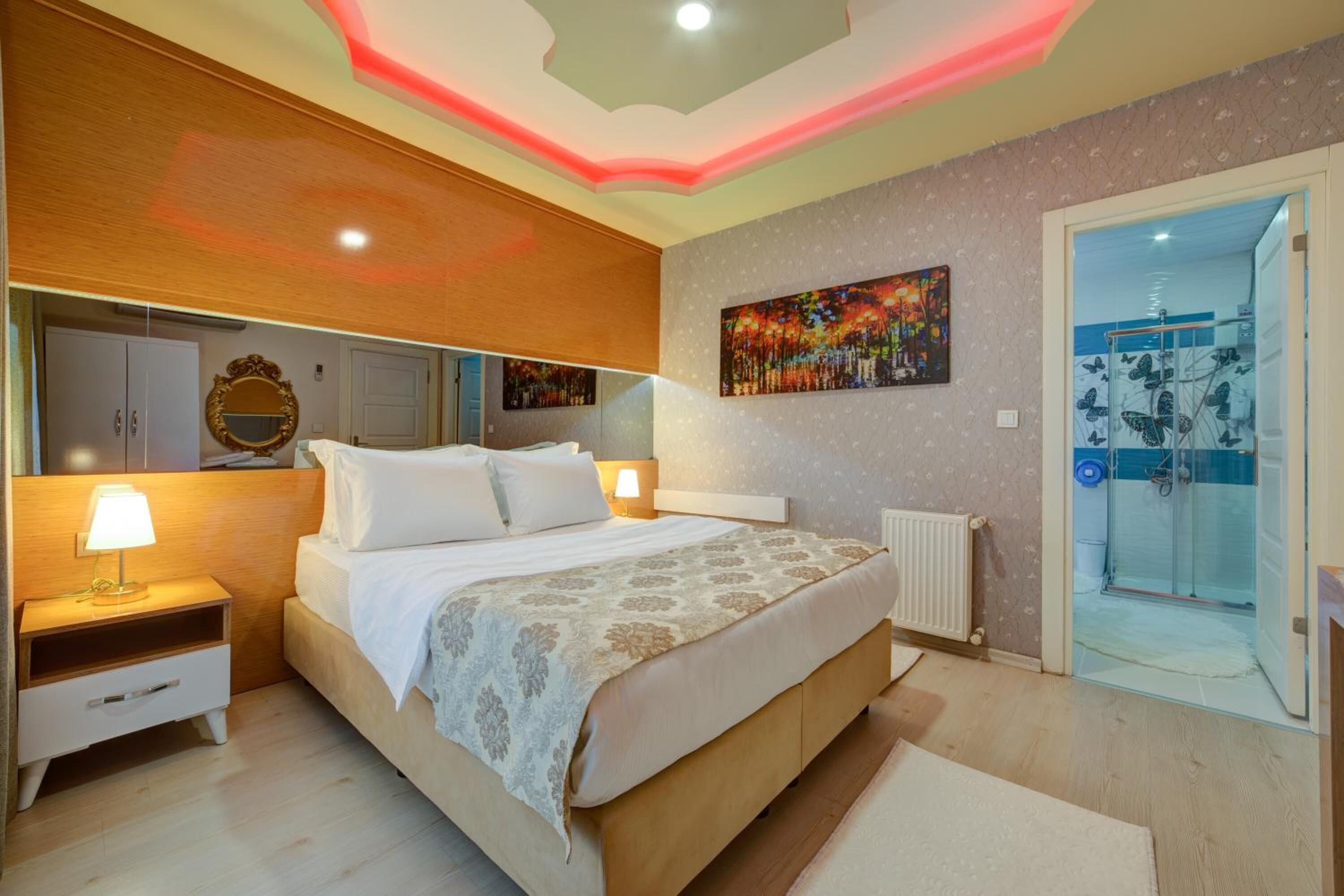 A bedroom with a bed, nightstands, a mirror, a painting, and a glass shower door.