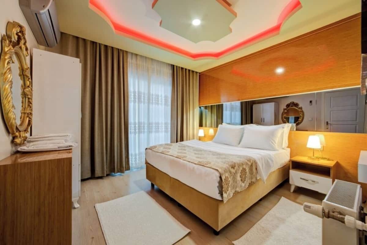 A hotel room with a bed, bedside tables, a mirror, curtains, and a ceiling with a unique design.
