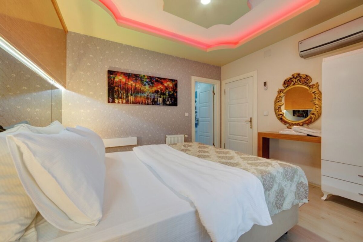 A bedroom with a bed, a painting on the wall, a mirror, and an air conditioning unit.