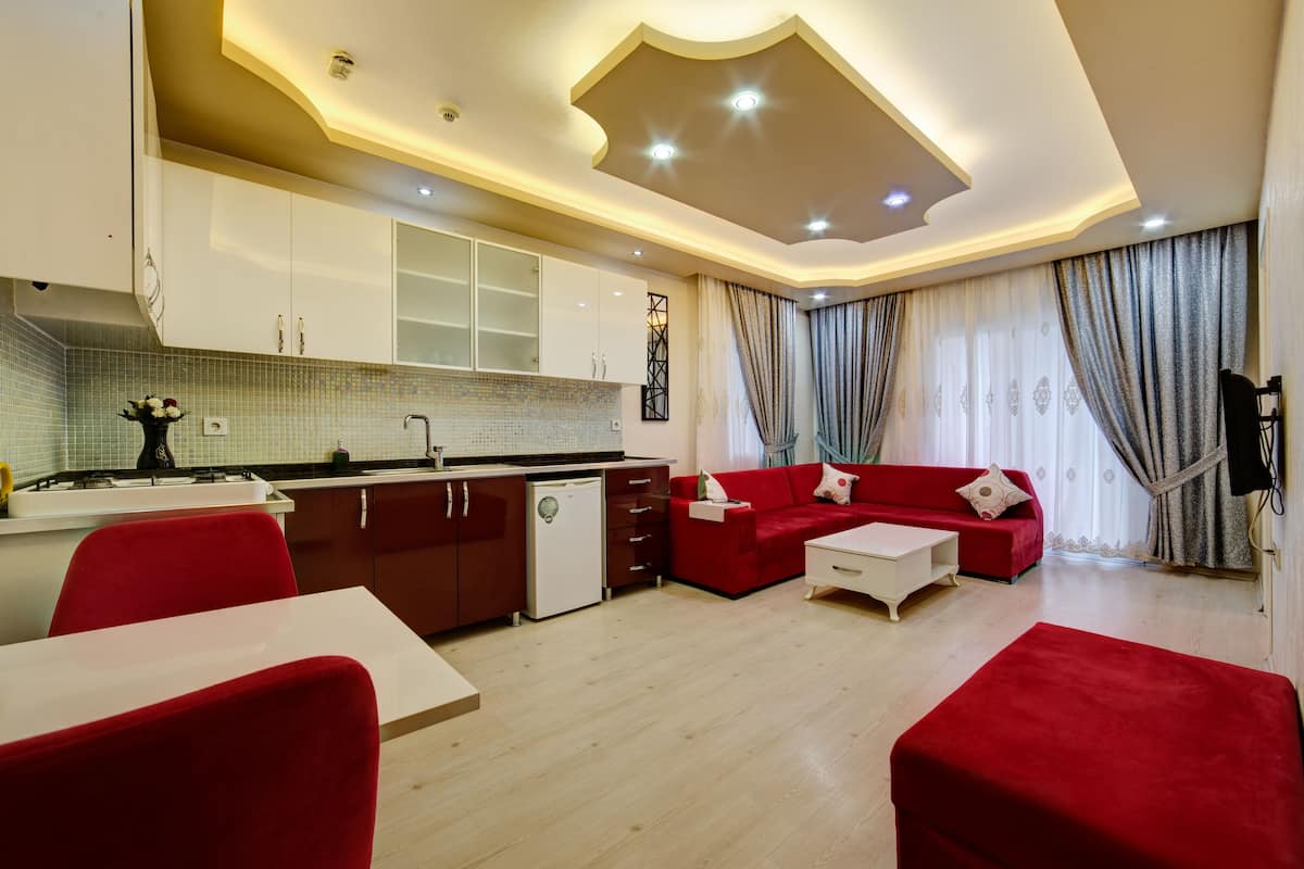 A modern living room with a red sofa, a dining table, and a kitchen area with white cabinets and a tiled backsplash.