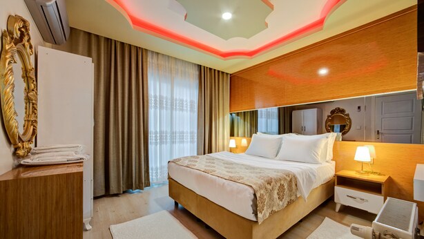 A modern hotel room with a large bed, bedside tables, a mirror, and a ceiling with a unique light fixture. - Mersin Vip House (Mezitli)