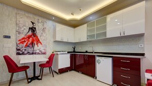 A modern kitchen with white and red cabinetry, a white dining table with red chairs, and a large abstract painting on the wall. - Mersin Vip House (Mezitli)