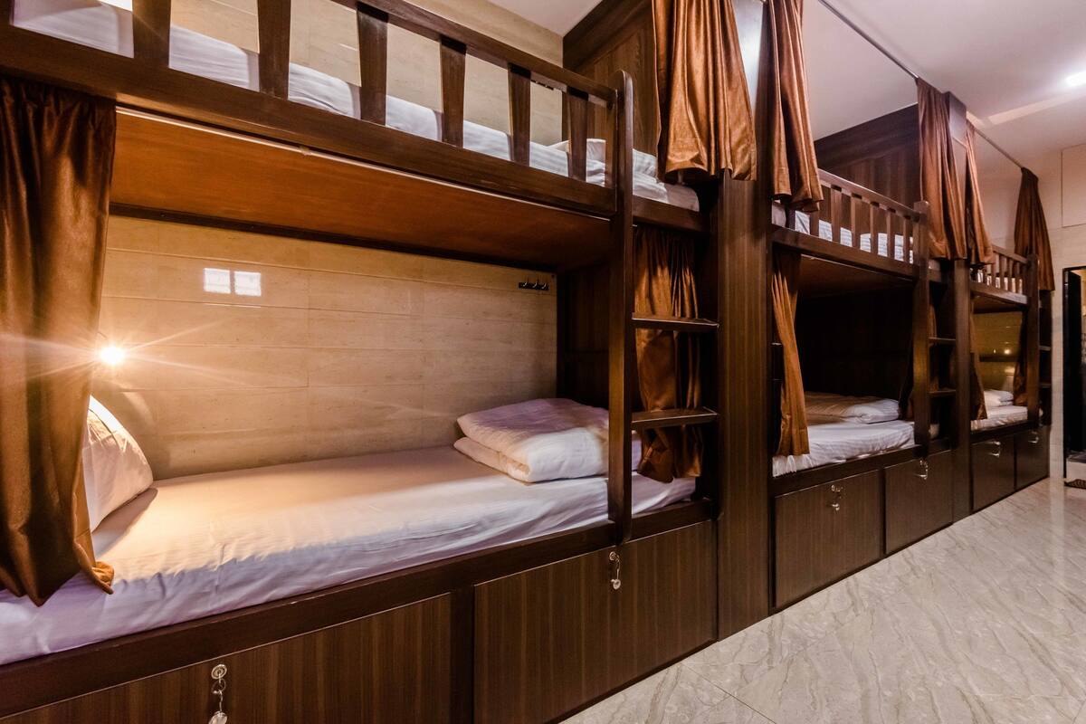 A bunk bed room with wooden headboards and curtains, a tiled floor, and a small window with sunlight.