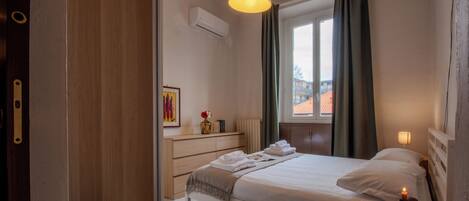 A hotel room with a bed, bedside table, lamp, and window with curtains.