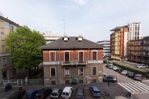A multi-story building with a flat roof, a balcony, and a parking area with cars. - Italianway   - Villoresi (Milan)