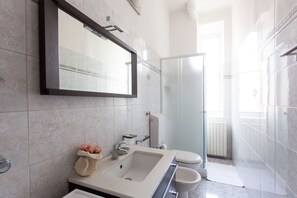 A modern bathroom with a large mirror, a sink, a toilet, and a glass shower enclosure. - Italianway   - Villoresi (Milan)
