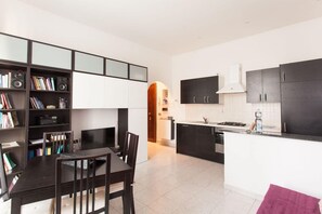 A modern kitchen with dark cabinetry, a central island, and a dining area with a table and chairs. - Italianway   - Villoresi (Milan)