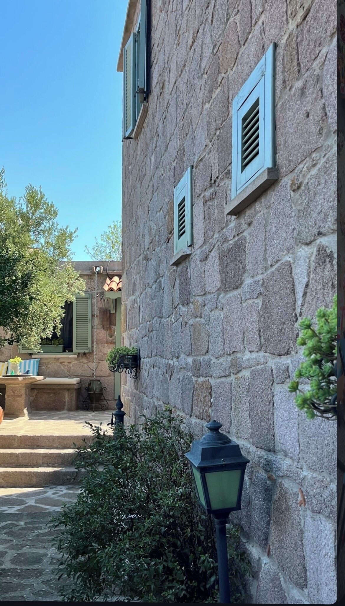 Un edificio de piedra con contraventanas, una escalera de piedra y un farol.