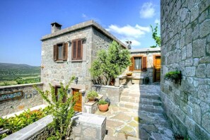 A stone building with wooden shutters, a small garden area with potted plants, and a view of the countryside. - Idasos Tasodalar (Ayvacik)