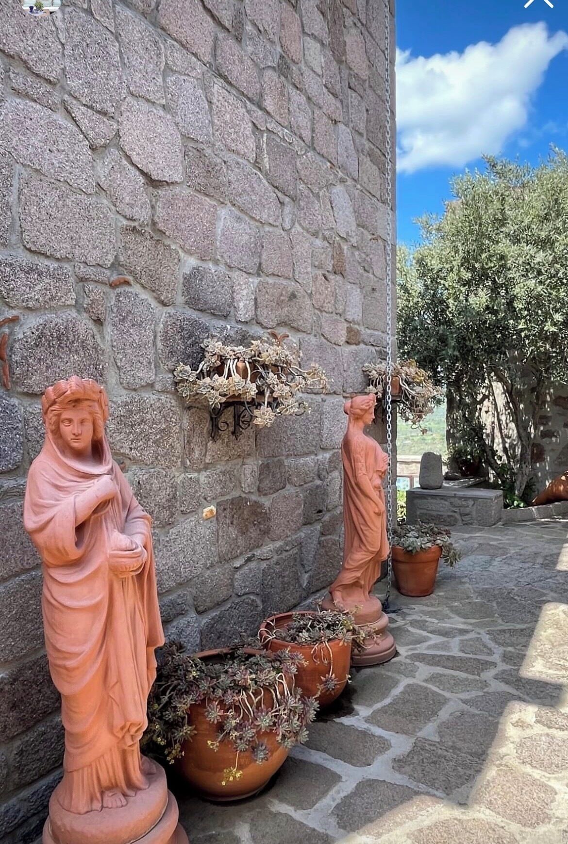 Tonfiguren, Topfpflanzen und eine Steinsäule.