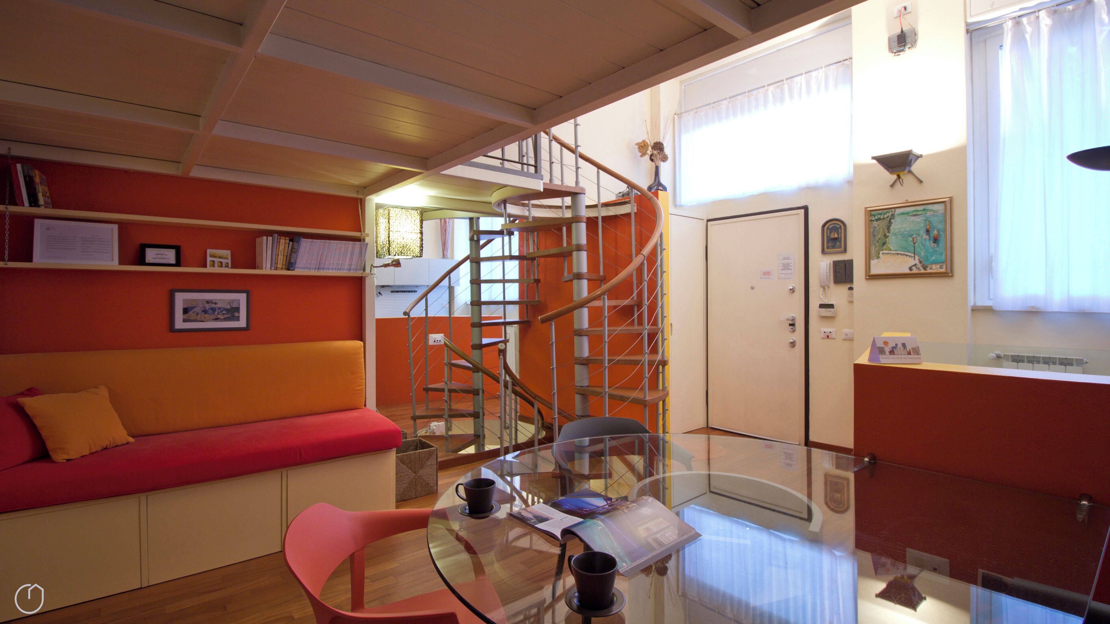 A compact living space with a sofa, a glass table with two cups, and a spiral staircase.