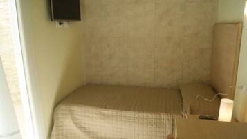 Una camera piccola con un letto singolo, una testiera semplice, un comodino e una lampada.