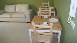 Una stanza piccola con un tavolo di legno apparecchiato per due persone, un divano bianco e un telefono appeso al muro.