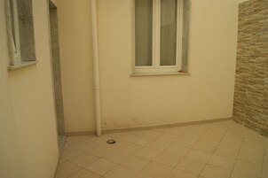 Um quarto pequeno e limpo, com soalho em azulejo, uma janela e uma parede com padrão texturizado.