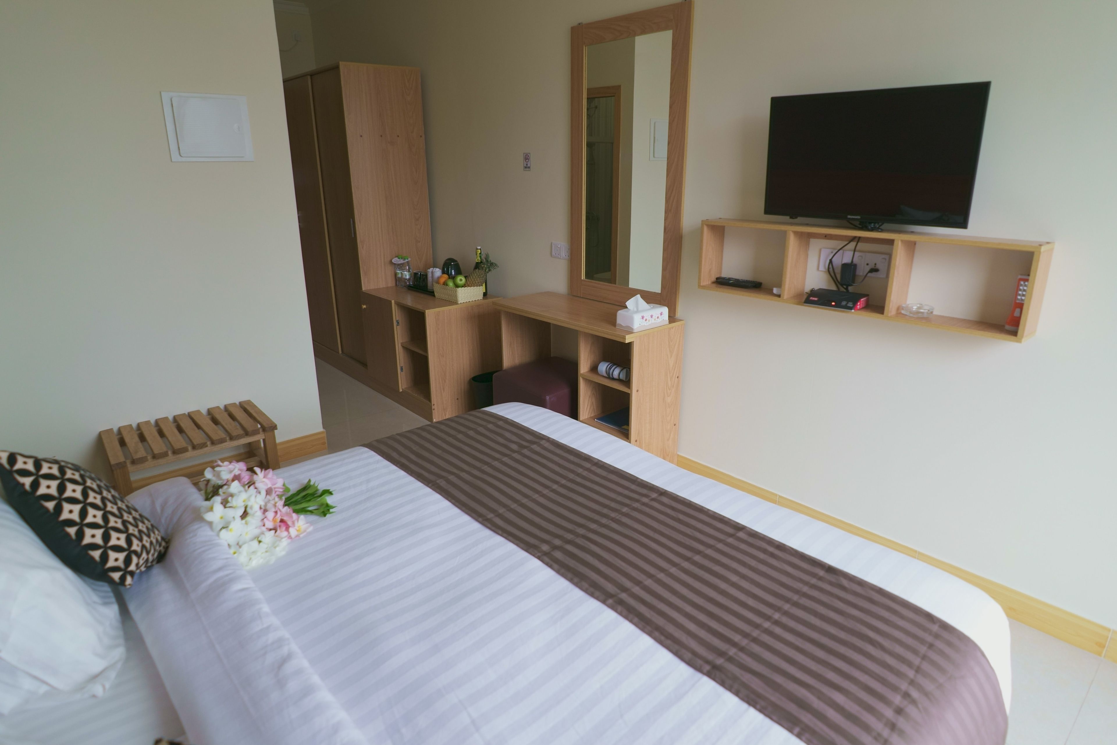 A hotel room with a bed, a wooden desk, a television, and a mirror.