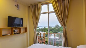 A hotel room with a TV on a shelf, a bed, a chair, and a balcony with a view of the sea. - Ocean Retreat & Spa (Guraidhoo)