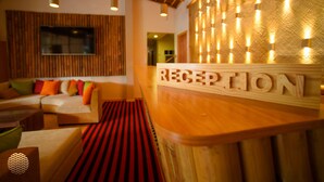 A reception area with a wooden reception desk labeled "RECEPTION," a sofa with colorful cushions, and a patterned carpet. - Ocean Retreat & Spa (Guraidhoo)