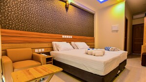 A hotel room with a bed, a wooden headboard, a small table, a chair, and a patterned wall. - Ocean Retreat & Spa (Guraidhoo)