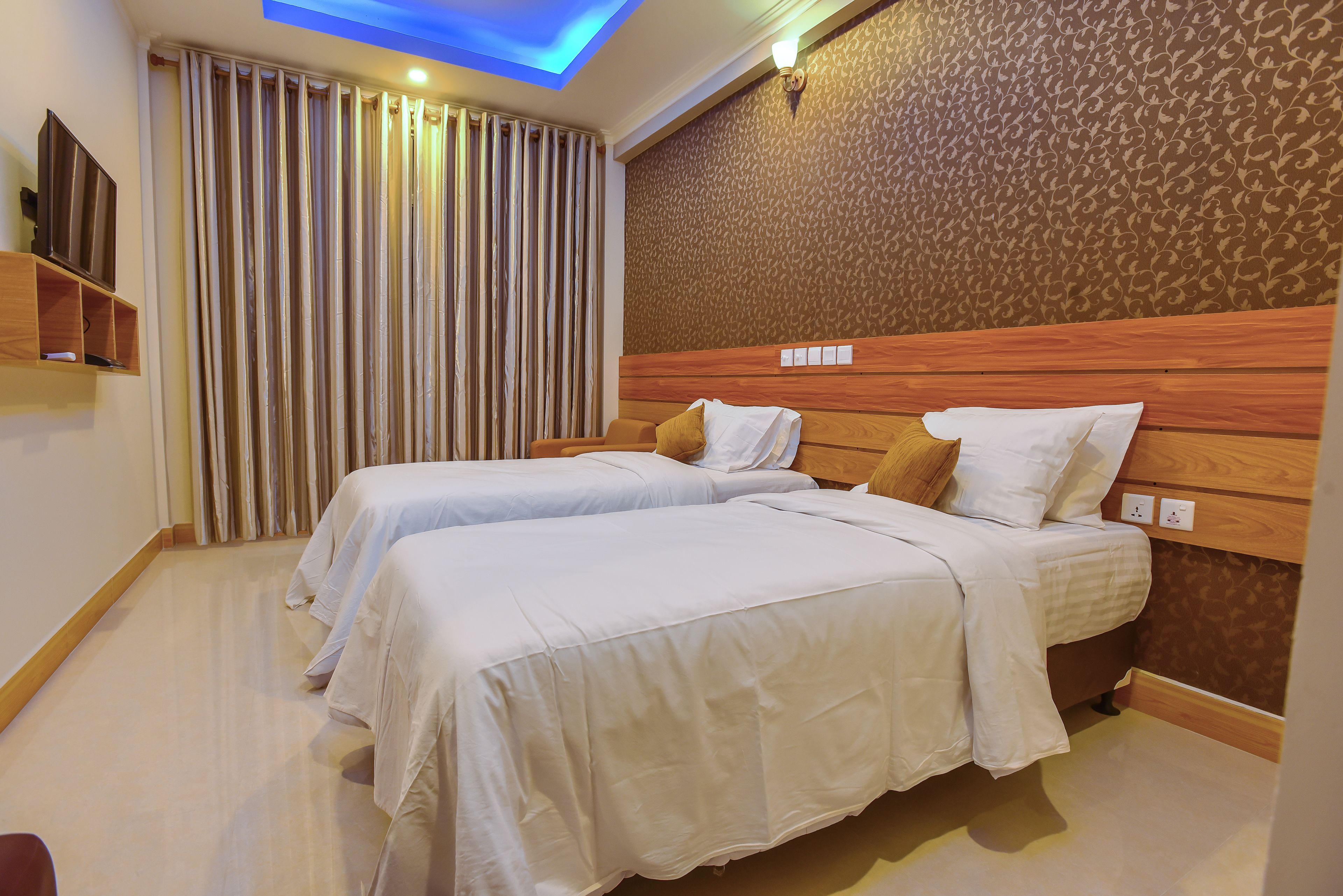 Ein Hotelzimmer mit zwei Betten, einem hölzernen Kopfteil, einer Wand mit Muster und einer Deckenleuchte.