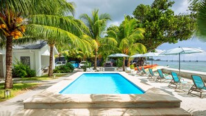 Una piscina con agua cristalina azul, rodeada de palmeras y sillones de descanso.