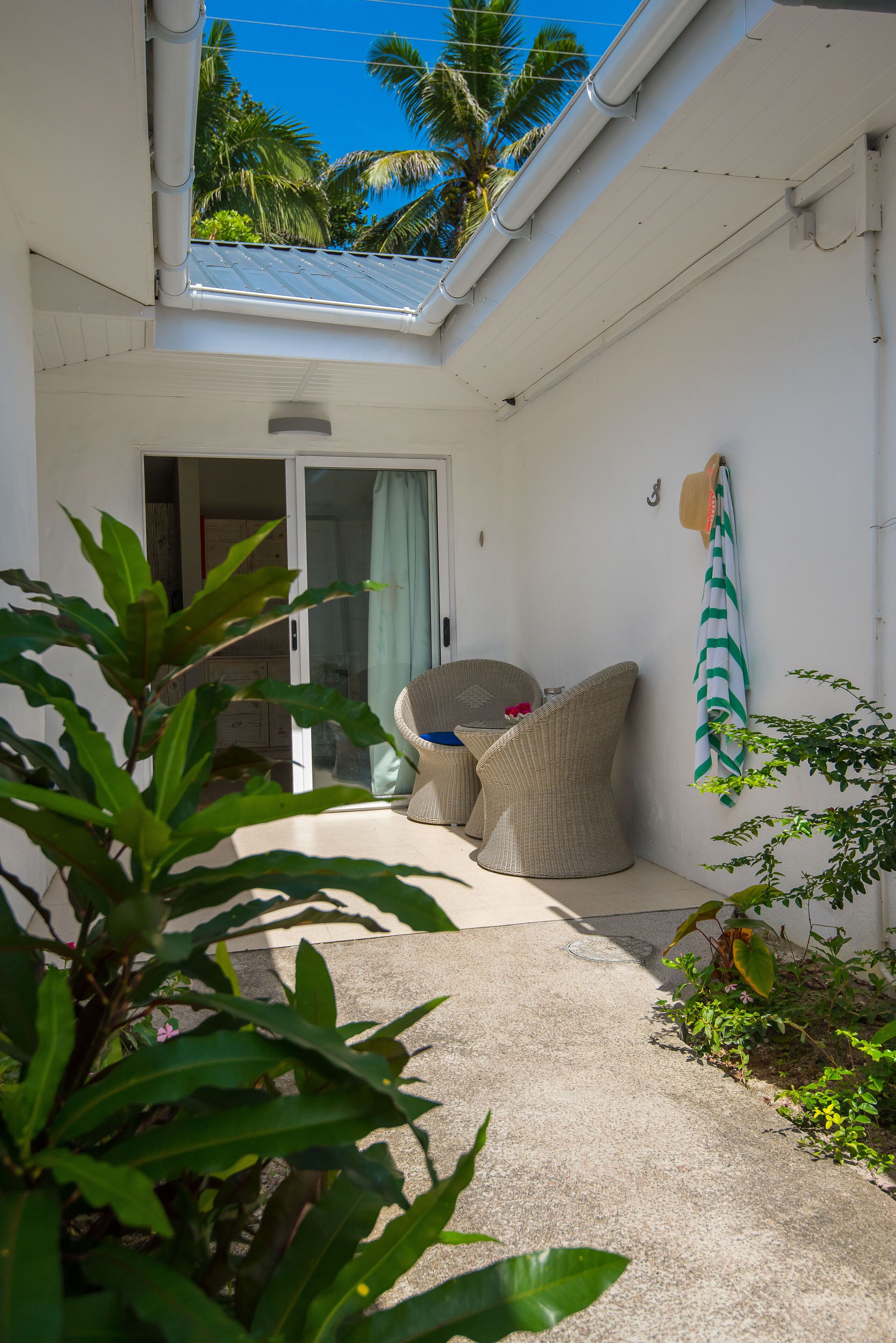 A small, enclosed patio area with a sliding glass door leading to a room, wicker furniture, a hat on the wall, and a view of palm trees.