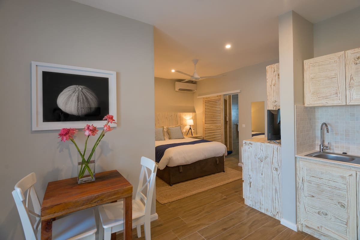 Un dormitorio con cama, mesita de noche y ventana. Incluye una kitchenette con lavaplatos y estufa.