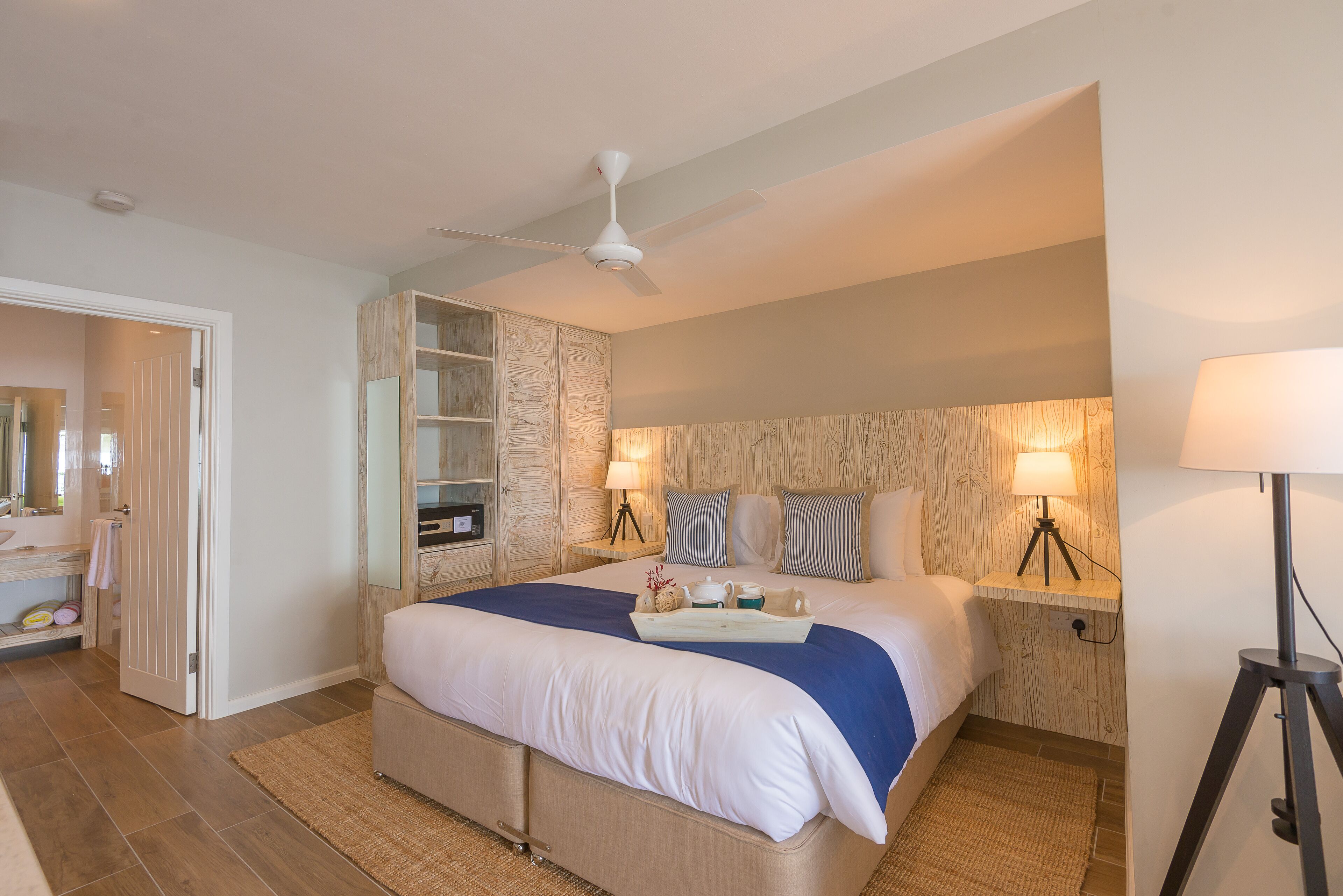 A hotel room with a large bed, a ceiling fan, a bedside table with a lamp, and a built-in wardrobe.