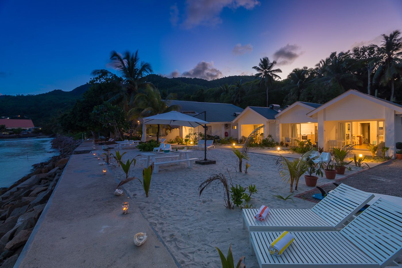 A beachfront resort with multiple villas, a sandy beach, and a rocky shoreline.