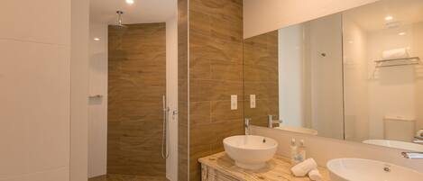 A modern bathroom with a wooden vanity, two sinks, a large mirror, and a walk-in shower.
