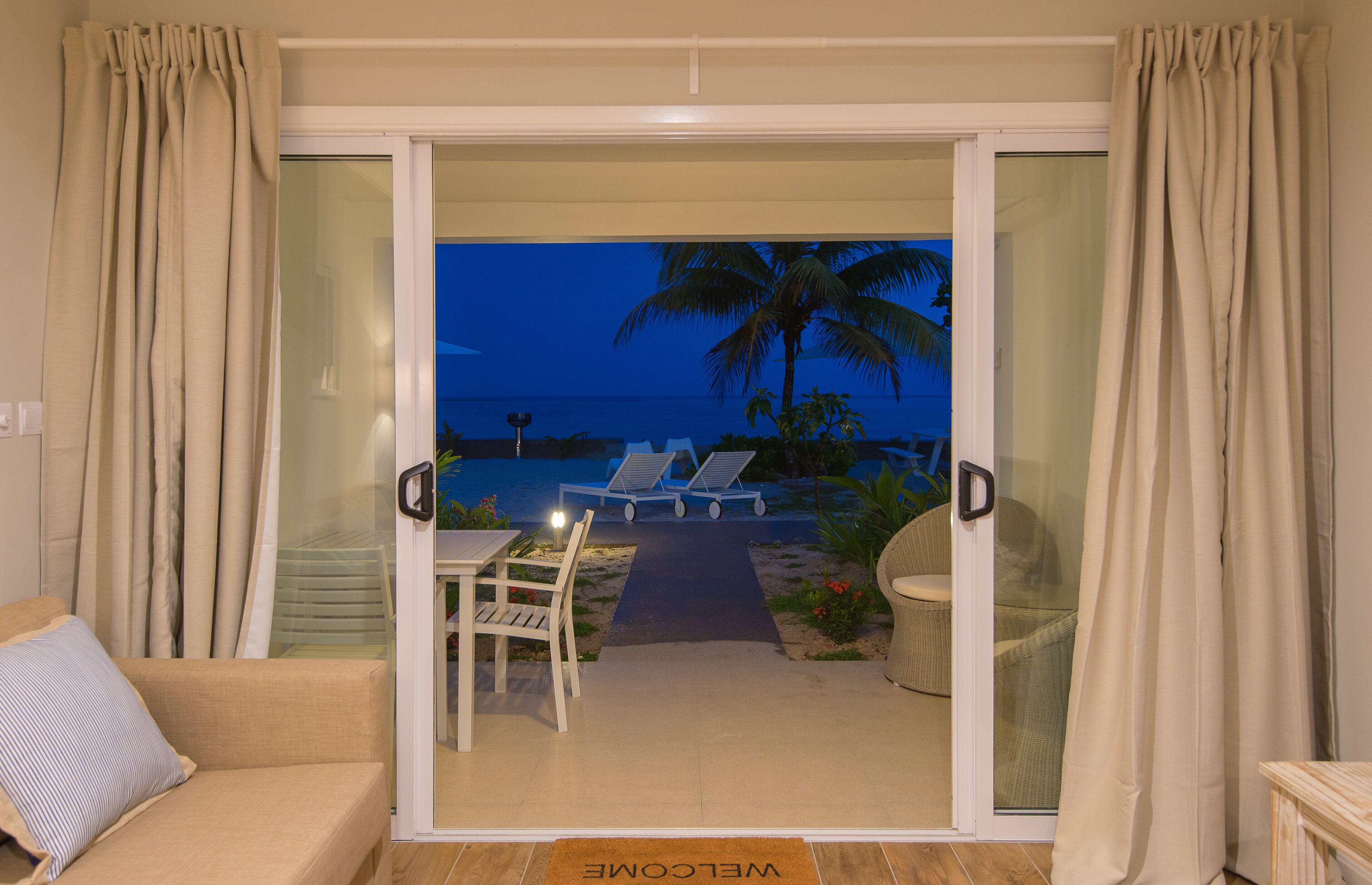 A room with a sliding glass door leading to a balcony with a view of the ocean and palm trees.