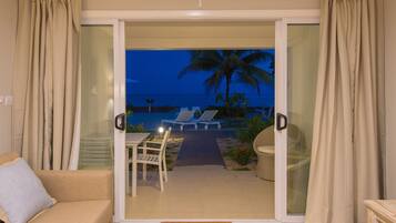 Ein Zimmer mit einer Schiebeglastür, die auf einen Balkon mit Blick auf das Meer und Palmen führt.