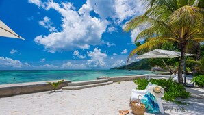 Una playa con una silla de descanso blanca, un sombrero de paja y un bolso de playa.