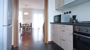 A modern kitchen with a microwave, coffee maker, and oven. There is a dining area with a table and chairs visible through an open door. - Italianway   - Zanella (Milan)