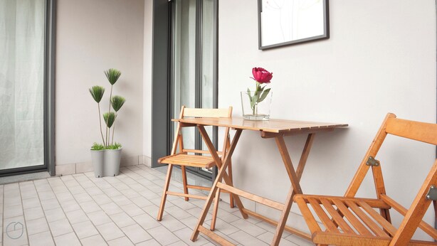 A small, modern outdoor seating area with a wooden table and chairs, a potted plant, and a framed picture on the wall. - Italianway   - Zanella (Milan)