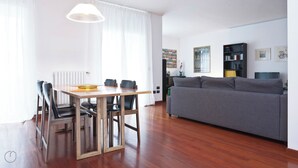 A modern living room with a wooden dining table, grey sofa, and a bookshelf. - Italianway   - Zanella (Milan)