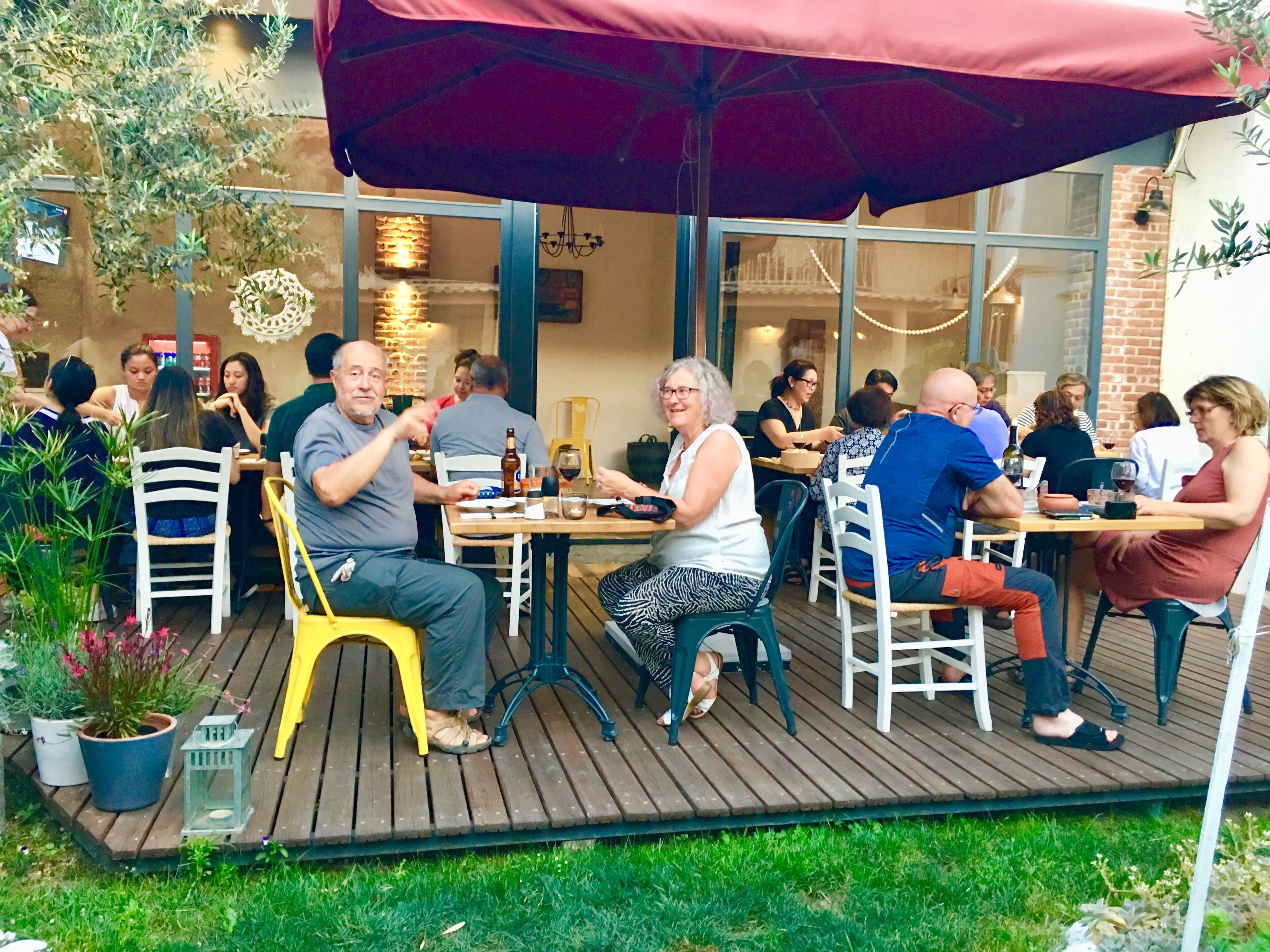 Un grupo de personas cenando al aire libre en un restaurante con terraza de madera, mesas y sillas.