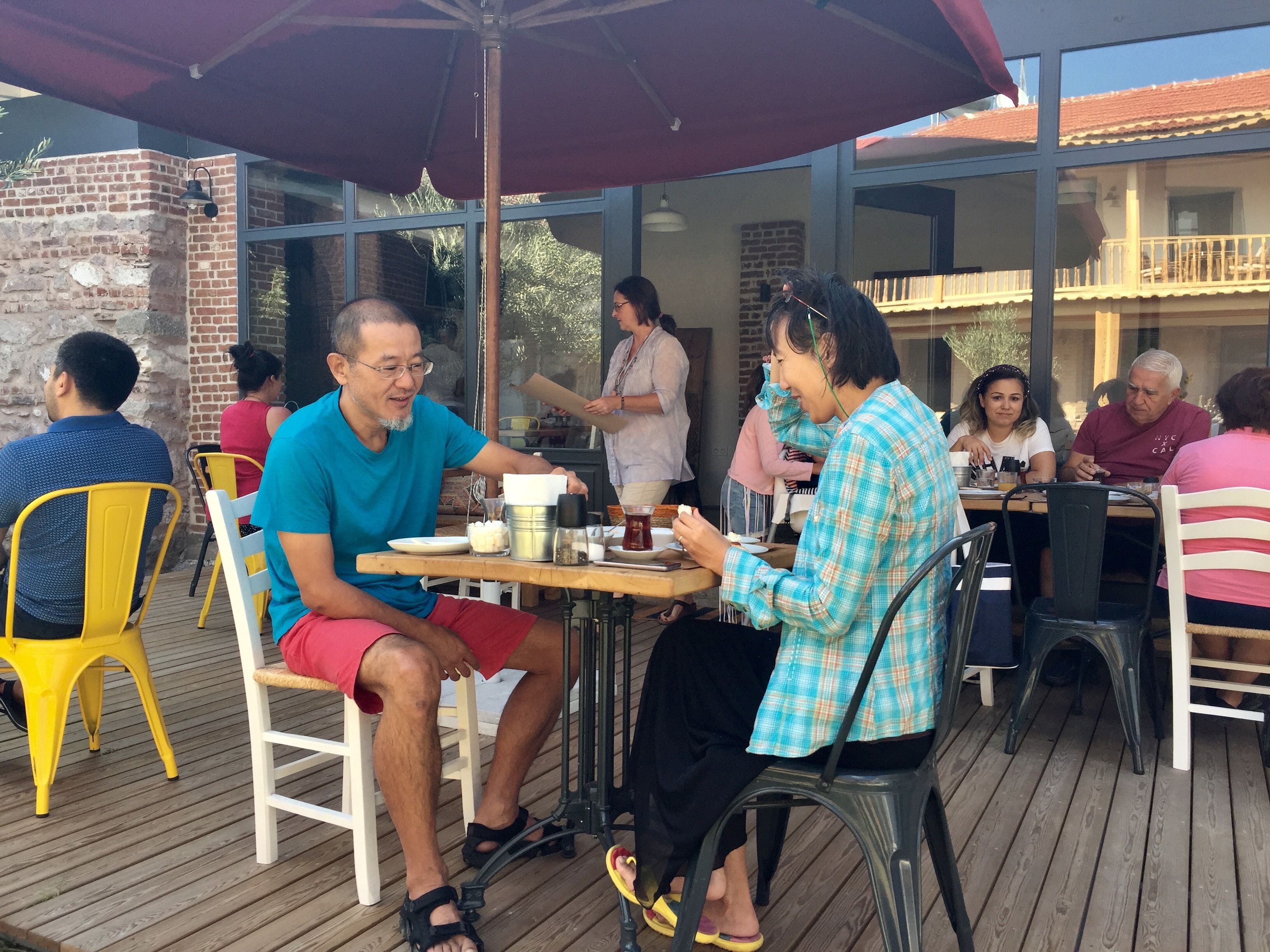 A wooden deck with outdoor seating, including yellow and white chairs, under a large umbrella.