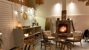 A cozy living room with wicker furniture, a fireplace, and a shelf with decorative items. - Attalos Suites Hotel (Bergama)