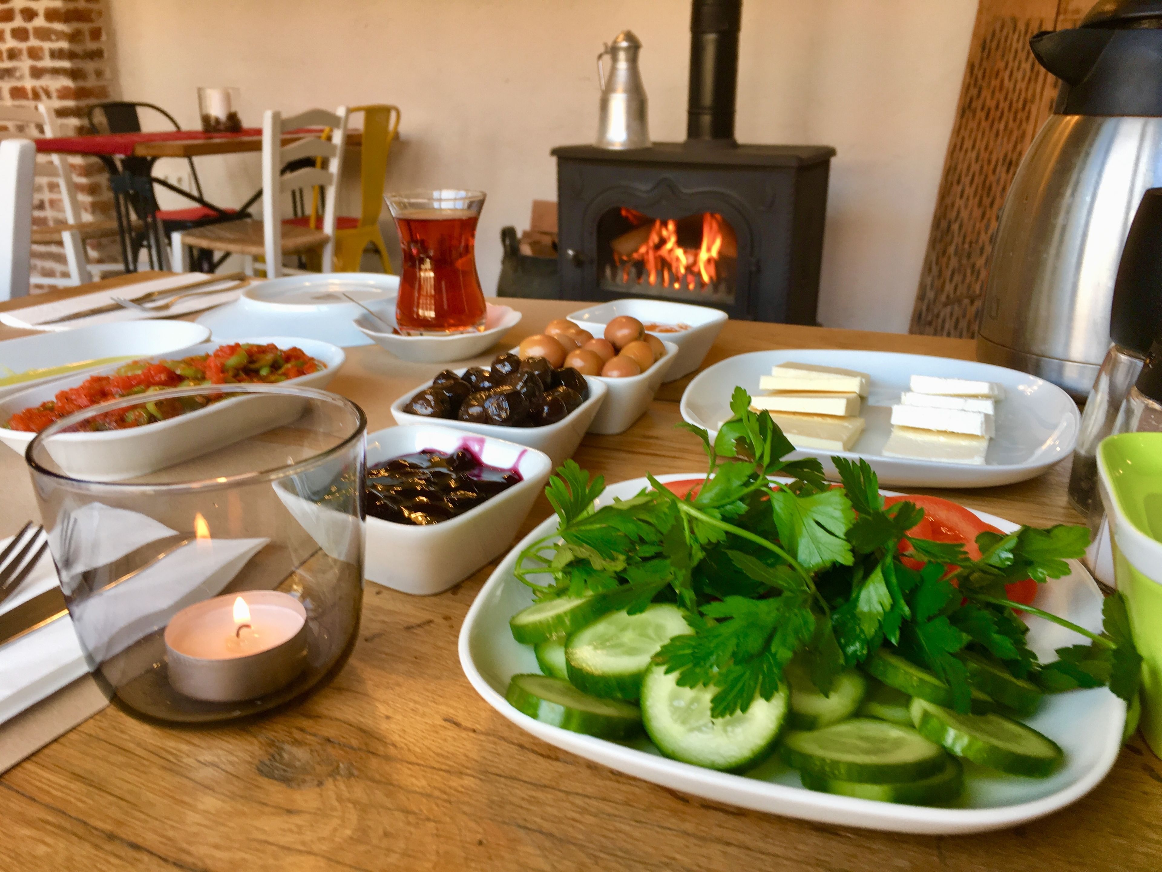 A dining table with various dishes, a candle, and a wood-burning stove in the background.