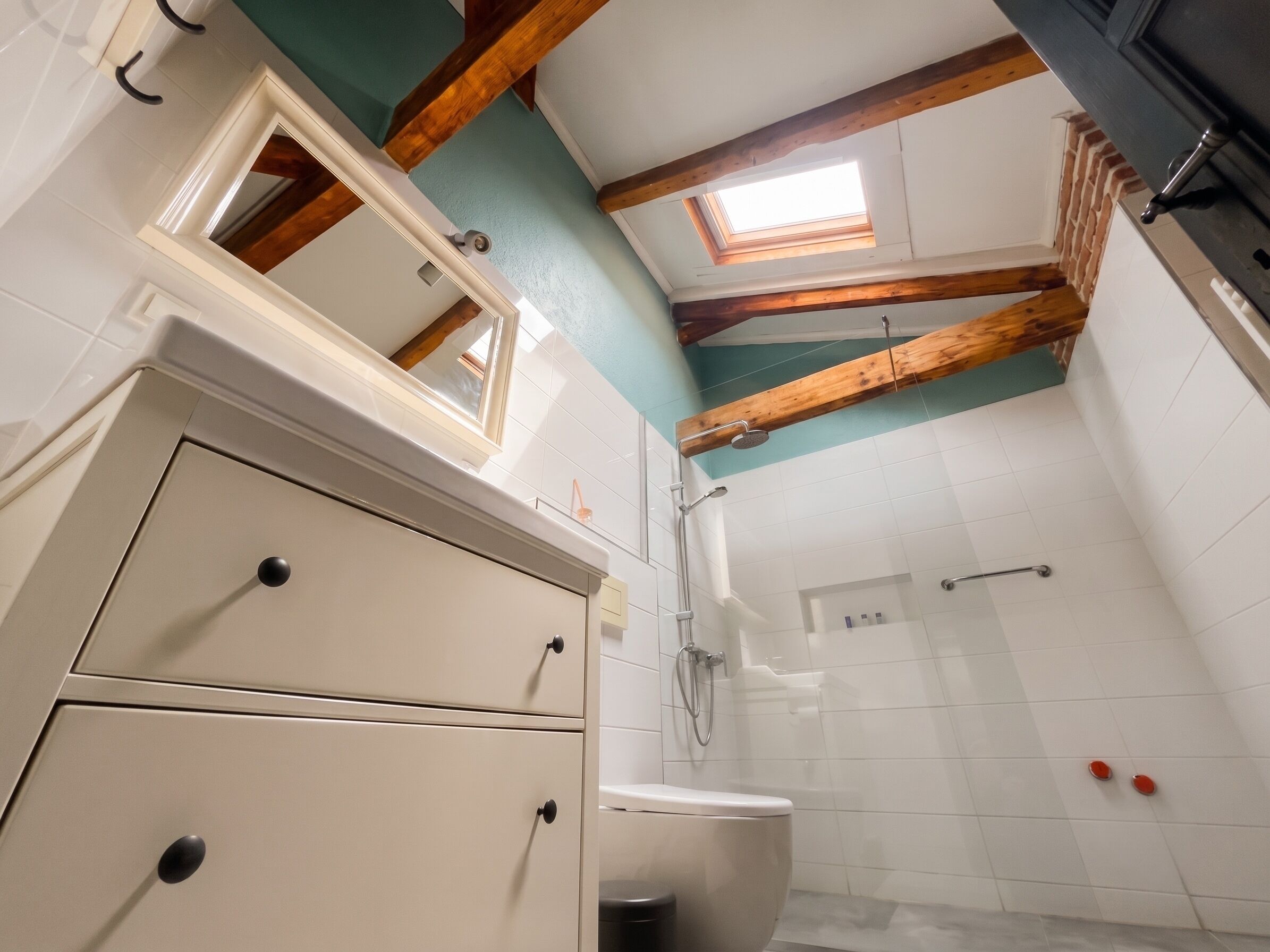 Un baño con tragaluz, vigas de madera, inodoro y ducha.