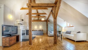 Ein großzügiges Loft mit Holzbalken, einem Fernseher, einer Couch und einem Essbereich.